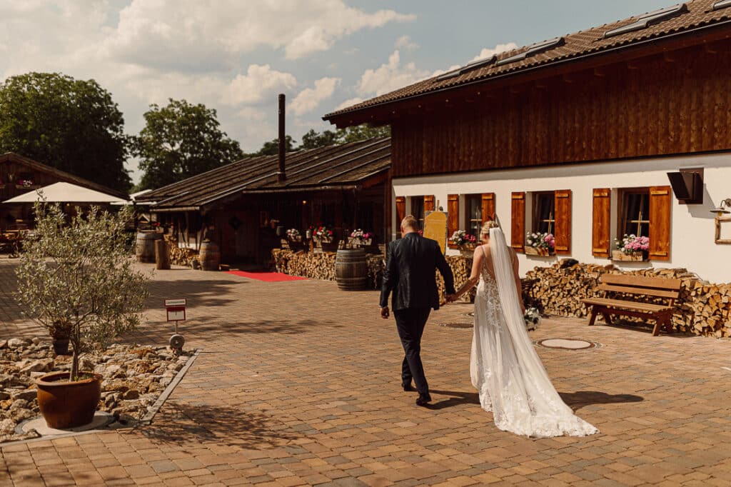 Brautpaar geht Hand in Hand über den Hof des Landguts Wickerbachmühle